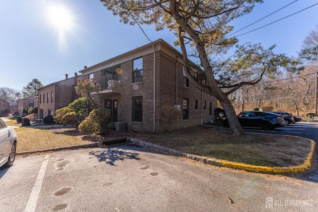 exterior space with a balcony, uncovered parking, central AC unit, and brick siding