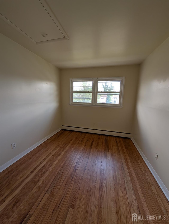 unfurnished room featuring attic access, a baseboard heating unit, dark wood-style floors, and baseboards