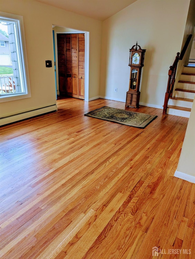 unfurnished room with light wood-style flooring, a baseboard heating unit, stairs, and baseboards