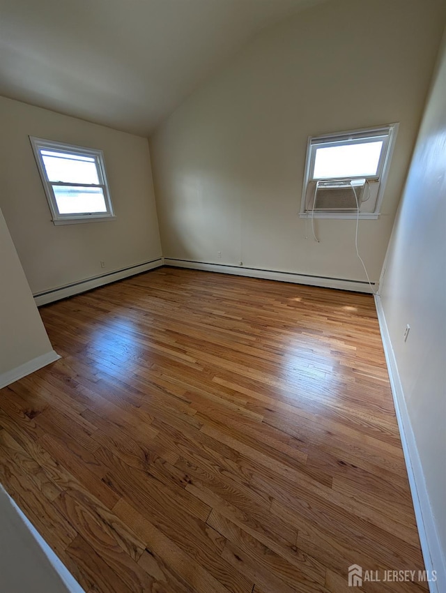 empty room featuring vaulted ceiling, wood finished floors, cooling unit, a baseboard radiator, and baseboards
