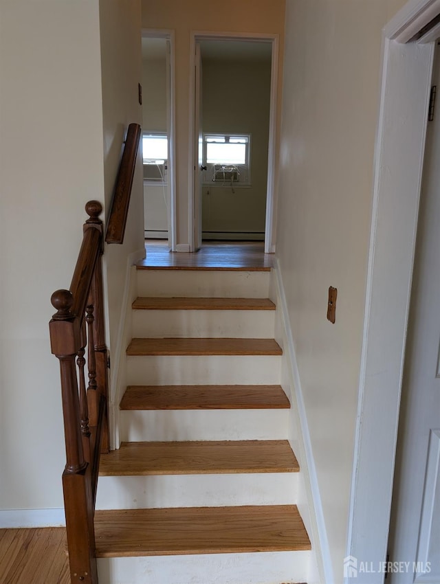stairs featuring a baseboard radiator, baseboards, and wood finished floors