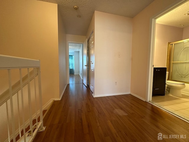 corridor with a textured ceiling, baseboards, and wood finished floors