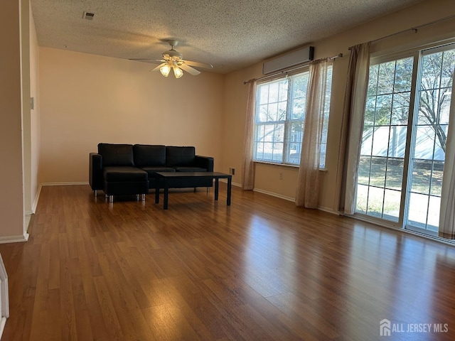 living room with a textured ceiling, wood finished floors, visible vents, baseboards, and a wall mounted AC