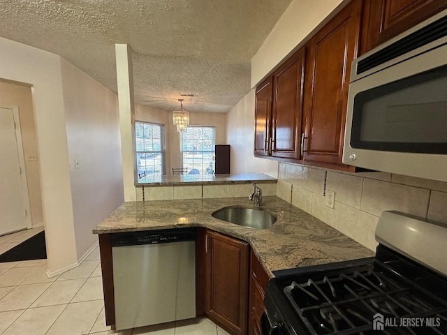 kitchen with light tile patterned floors, light stone counters, a peninsula, stainless steel appliances, and a sink