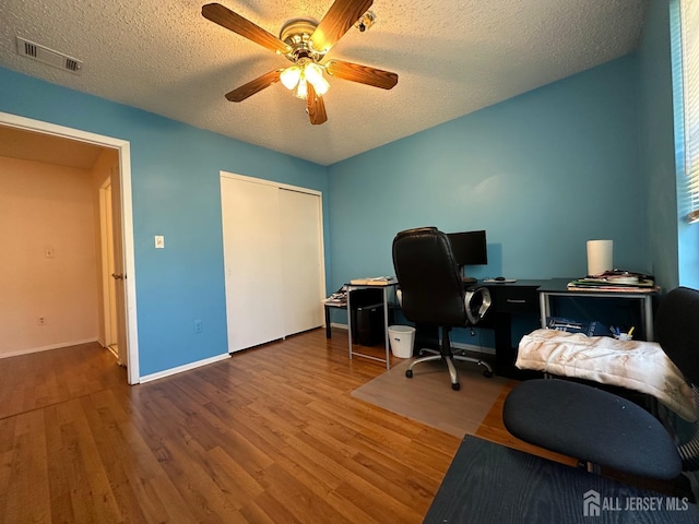 office space with a ceiling fan, visible vents, a textured ceiling, and wood finished floors