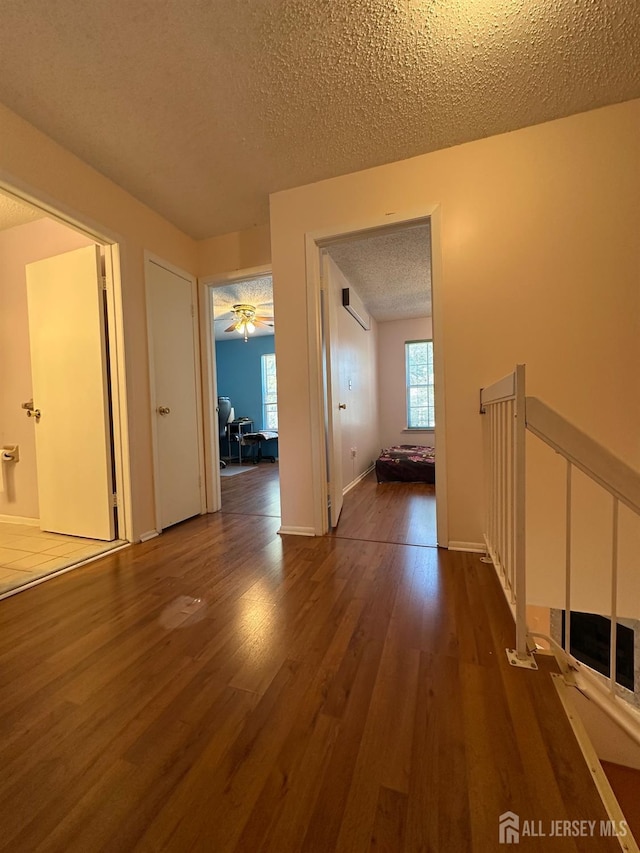 hall featuring a textured ceiling, baseboards, dark wood-style flooring, and a wall mounted air conditioner