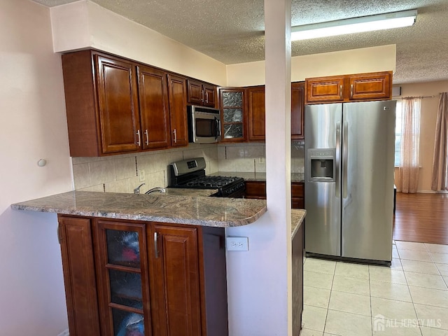 kitchen with a peninsula, glass insert cabinets, stainless steel appliances, and decorative backsplash