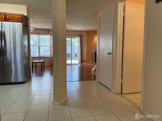 kitchen featuring light tile patterned floors, baseboards, brown cabinets, freestanding refrigerator, and a textured ceiling