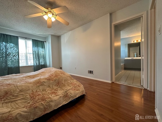 bedroom featuring visible vents, connected bathroom, a textured ceiling, wood finished floors, and baseboards