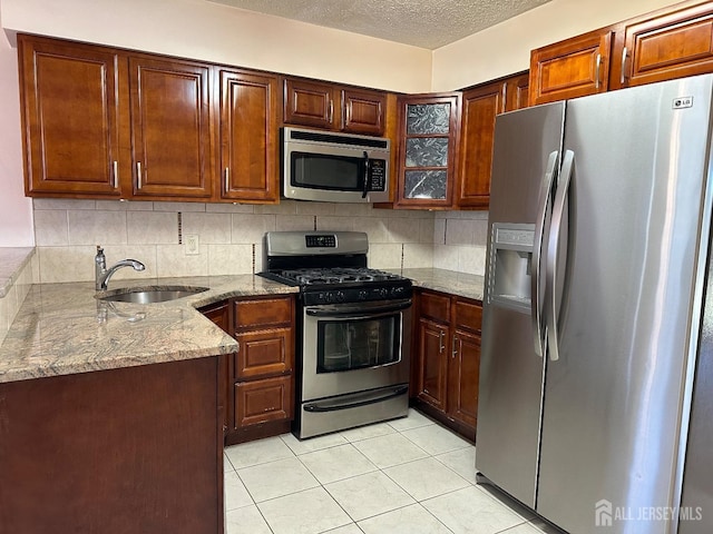 kitchen with glass insert cabinets, appliances with stainless steel finishes, light stone countertops, a textured ceiling, and backsplash