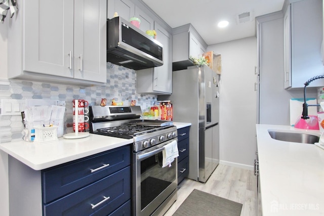 kitchen featuring stainless steel appliances, tasteful backsplash, blue cabinetry, sink, and light hardwood / wood-style flooring