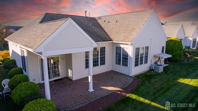 back house at dusk featuring cooling unit, a patio area, and a yard