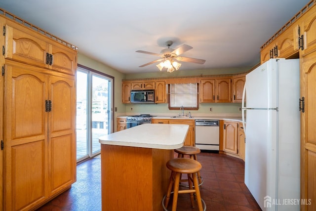 kitchen with sink, white appliances, a breakfast bar, ceiling fan, and a kitchen island