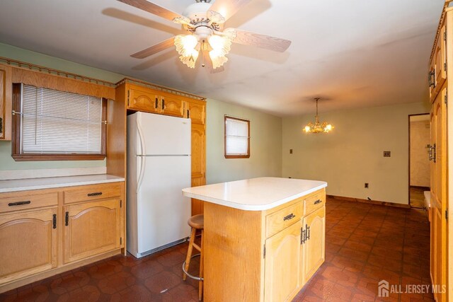 kitchen featuring ceiling fan with notable chandelier, decorative light fixtures, a kitchen bar, white fridge, and a center island