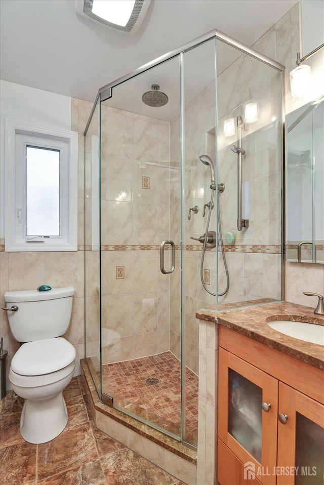 bathroom featuring tile walls, a shower stall, toilet, and vanity