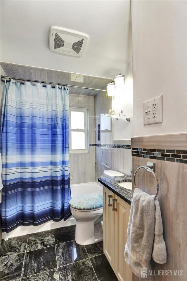 bathroom featuring tile walls, vanity, shower / tub combo, toilet, and marble look tiles