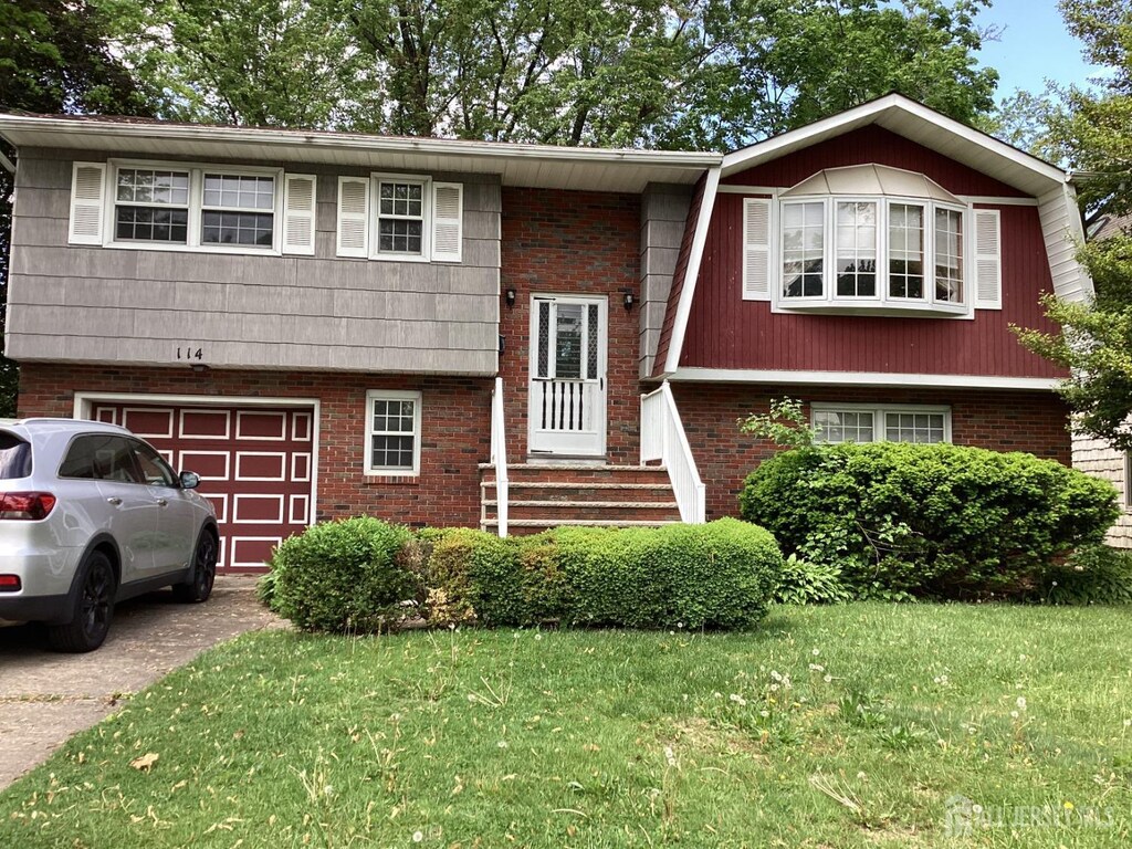 split foyer home with an attached garage, a front yard, driveway, and brick siding