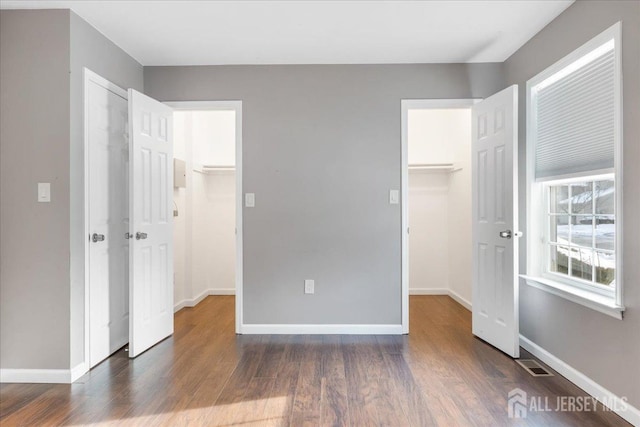 unfurnished bedroom with dark wood-type flooring, a walk in closet, visible vents, and baseboards