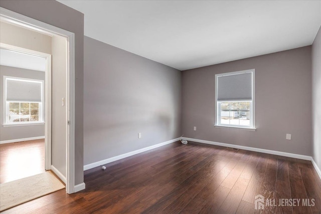 unfurnished room with dark wood-style flooring, visible vents, and baseboards