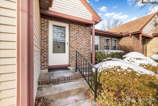 snow covered property entrance with brick siding