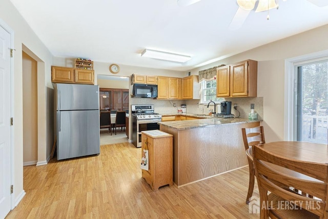 kitchen with sink, kitchen peninsula, stainless steel appliances, light hardwood / wood-style floors, and decorative backsplash