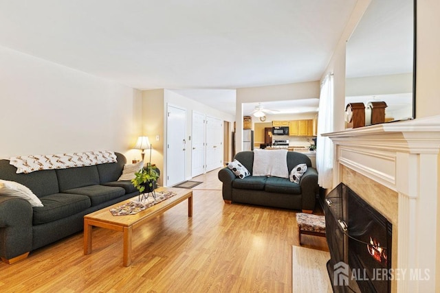 living area with light wood-type flooring, a high end fireplace, and a ceiling fan