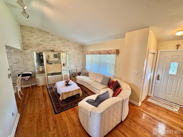 living area featuring brick wall, healthy amount of natural light, wood finished floors, lofted ceiling, and baseboards