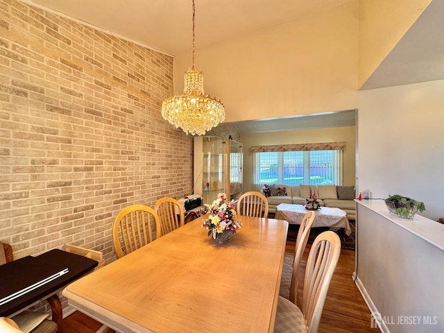 dining space featuring brick wall, a chandelier, wood finished floors, and a high ceiling