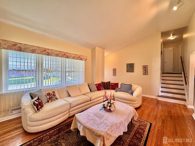 living room featuring wood finished floors, vaulted ceiling, baseboards, and stairway