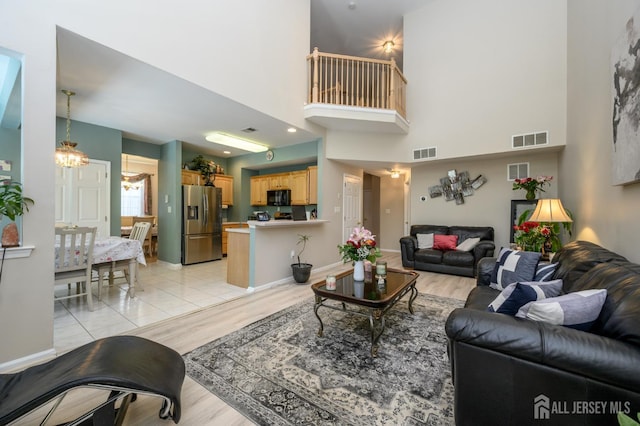 living area with a chandelier, light wood-style floors, a towering ceiling, and baseboards