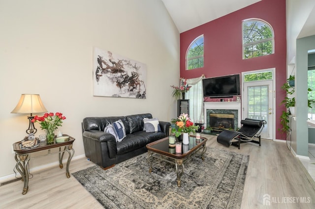 living room featuring wood finished floors, high vaulted ceiling, healthy amount of natural light, a premium fireplace, and baseboards