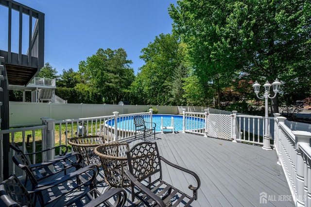 view of swimming pool with a fenced backyard, a deck, and view of wooded area