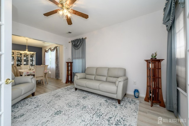 living area with light wood-style floors, ceiling fan, a chandelier, and baseboards