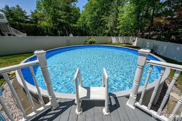 view of swimming pool featuring a fenced backyard, a deck, and view of wooded area