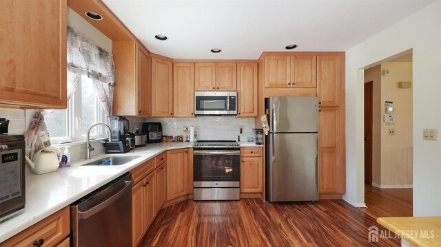 kitchen with dark wood-style floors, appliances with stainless steel finishes, a sink, light countertops, and backsplash