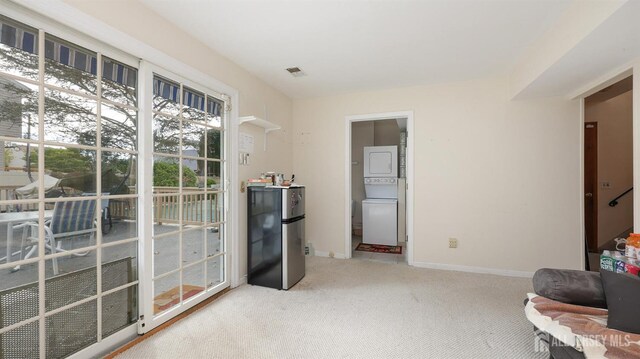 sitting room with baseboards, visible vents, stacked washer / drying machine, and light colored carpet