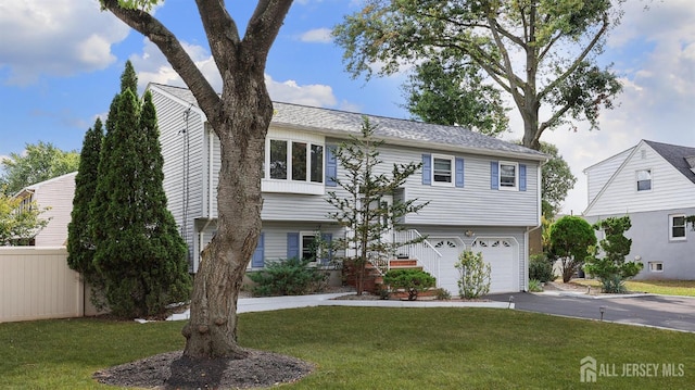 bi-level home with a garage, fence, a front lawn, and aphalt driveway