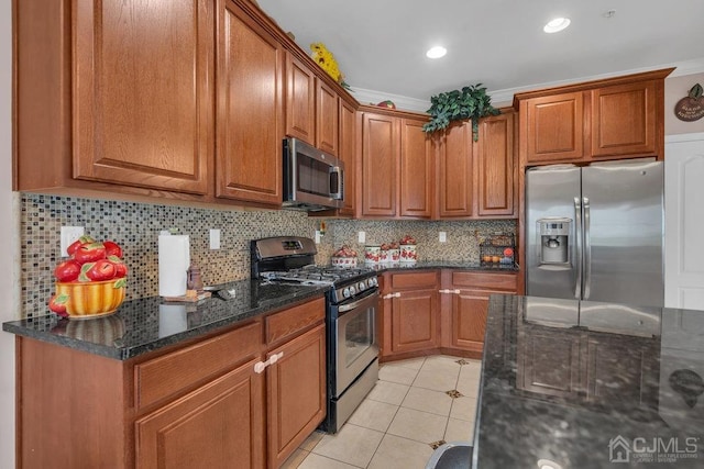 kitchen with appliances with stainless steel finishes, light tile patterned flooring, dark stone countertops, and tasteful backsplash