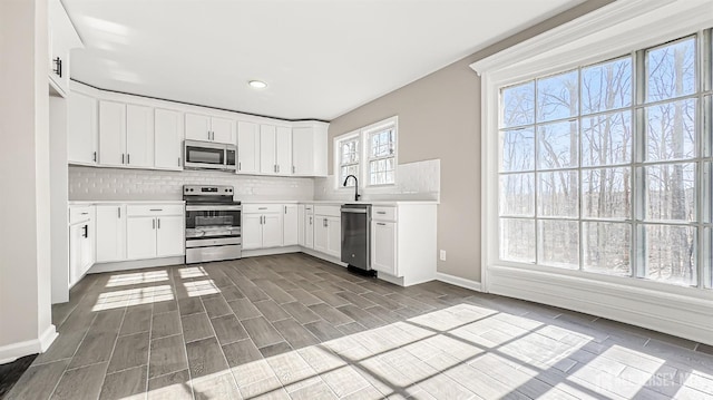 kitchen with appliances with stainless steel finishes, backsplash, baseboards, light countertops, and white cabinets