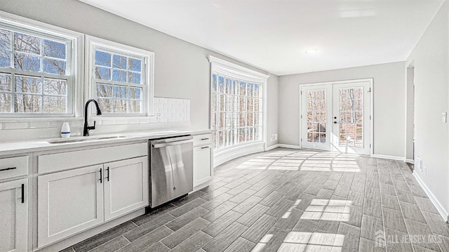 kitchen with white cabinets, dishwasher, a sink, light countertops, and backsplash