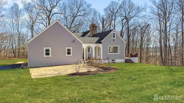 view of front of property featuring roof with shingles, a chimney, a front lawn, and a patio