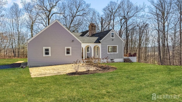 back of house featuring a chimney, a yard, and a shingled roof