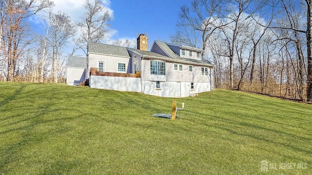 back of house with a chimney and a lawn