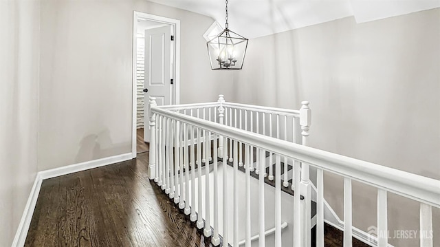 hallway with dark wood-type flooring, baseboards, a notable chandelier, and an upstairs landing