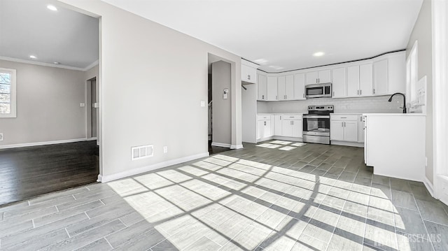 kitchen featuring appliances with stainless steel finishes, white cabinets, light countertops, light wood-style flooring, and baseboards