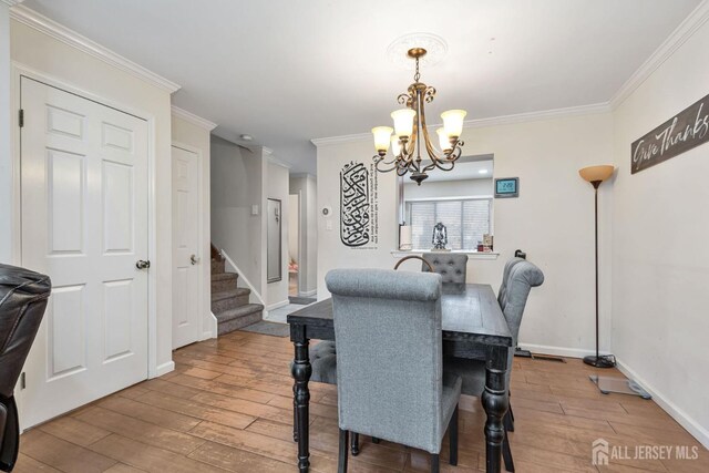 dining space with hardwood / wood-style flooring, crown molding, and an inviting chandelier