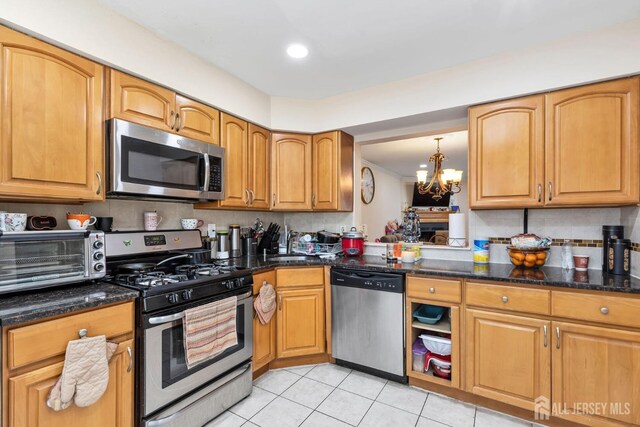 kitchen with light tile patterned floors, stainless steel appliances, dark stone counters, a chandelier, and pendant lighting