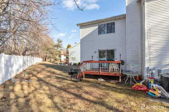 rear view of property featuring central AC unit, a wooden deck, and a lawn