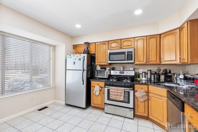 kitchen featuring light tile patterned floors, appliances with stainless steel finishes, dark stone counters, and sink