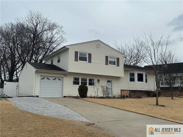 tri-level home featuring a garage, a gate, driveway, and a front lawn